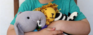 child hugging three knit animals. one elephant, lion, and zebra