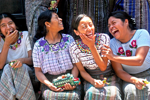 4 women artisans in Guatemala sitting each holding their craft, smiling and laughing together.