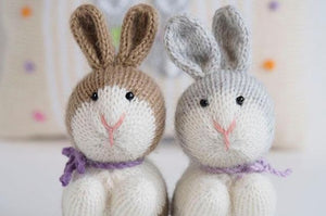 2 knitted bunnies next to each other. one brown and white, and the other gray and white.